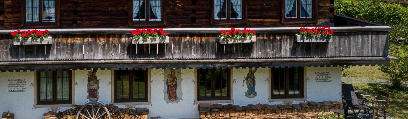 Bemaltes Erdgeschoss des Gasperhofs mit Heiligenfiguren, darüber die Laube mit Geranien