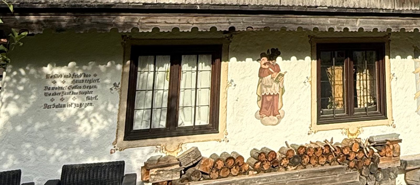 Weiß verputztes Erdgeschoss mit Hausspruch in Frakturschrift, Fenster mit Holzrahmen und eine gemalte Heiligenfigur