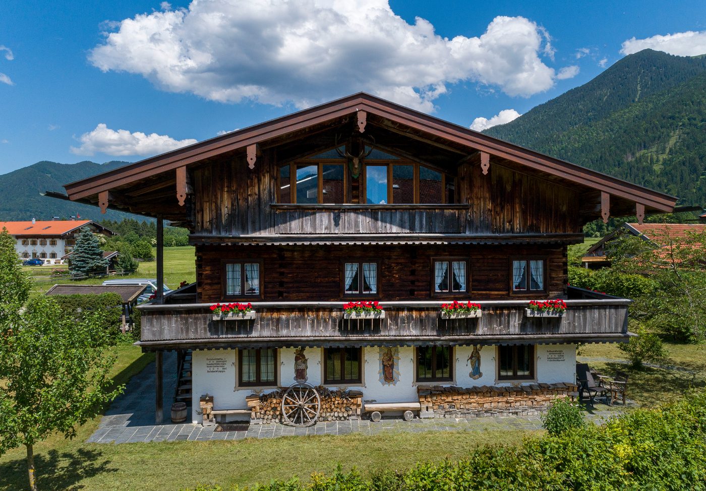 Die Hausfront des Gasperhofs mit Laube, Geranien und bemaltem Erdgeschoss, dahinter der Wallberg